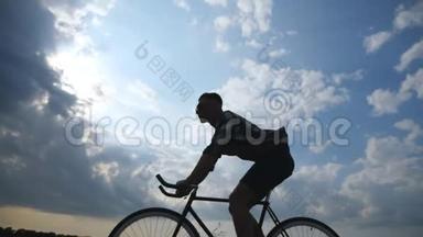 年轻人骑着老式自行车的剪影，背景是美丽的日落天空。 骑自行车的人